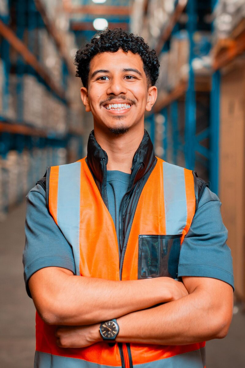 Varastotyöntekijä seisoo hyllyjen välissä kädet ristissä.