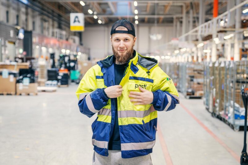 Lajittelija Joona Natunen seisoo Postin logistiikkakeskuksessa ja katsoo suoraan kameraan.