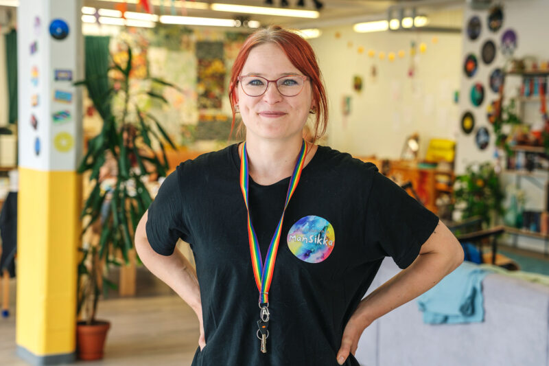 Hanketyöntekijä Elisa Kivinen seisoo värikkäästi sisustetussa kulttuuripajassa kädet lanteilla ja katsoo suoraan kameraan.